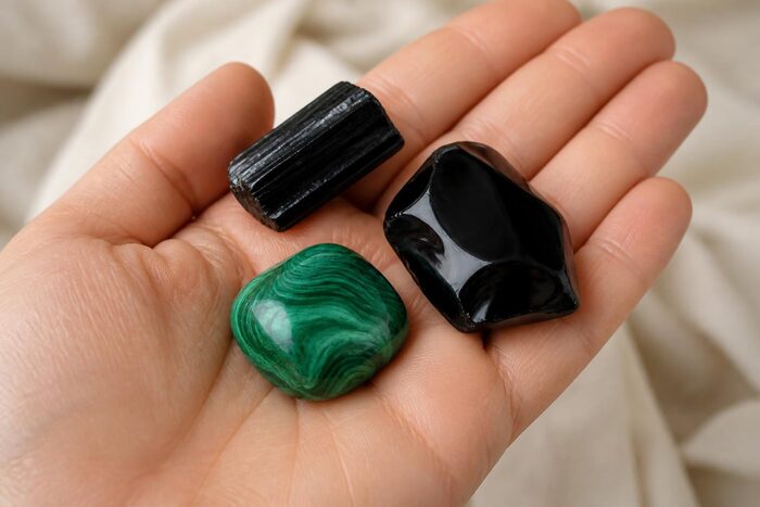 Turmalină neagră brută, obsidian negru lustruit și malachit verde ținute în palmă